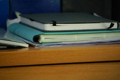 A stack of notebooks and folders sits on the wooden desk, catching the morning  Stock Photos