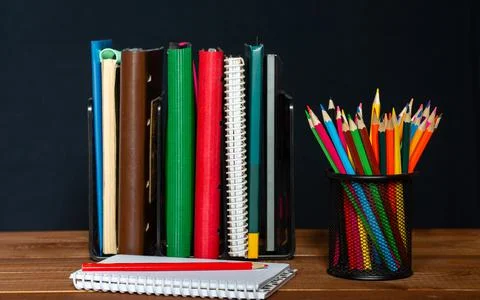 A stack of notebooks, a jar of pencils and a notepad on the table. Stock Photos