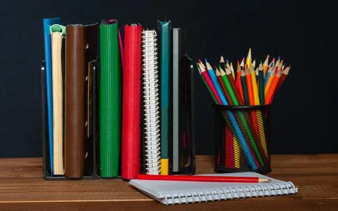 A stack of notebooks, a jar of pencils and a notepad on the table. Stock Photos