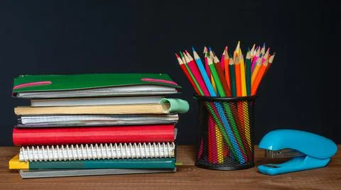 A stack of notebooks, a jar of pencils and a stapler on the table. Stock Photos