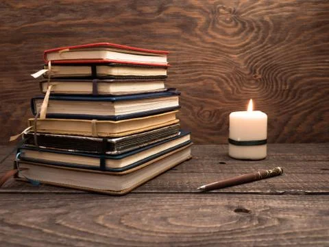 A stack of notebooks, a pen and a candle on a wooden table Stock Photos