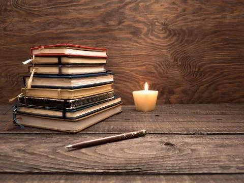 A stack of notebooks, a pen and a candle on a wooden table Stock Photos