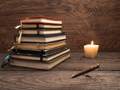A stack of notebooks, a pen and a candle on a wooden table Stock Photos