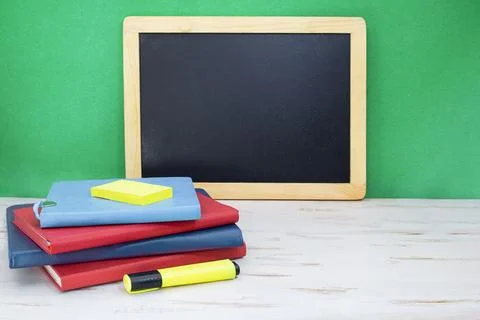 Stack of notepads with marker on white table. Black board on green background Foto stock