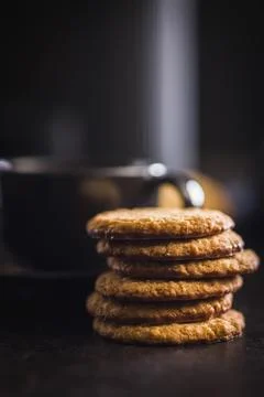 Stack of oatmeal cookies on black table with some placed beside it in a kit.. 스톡 사진