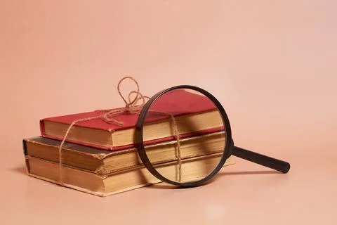 A stack of old battered books tied with a jute rope and a magnifying glass Stock Photos