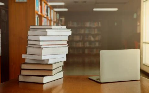 Stack of old books and laptop computer on desk in library background. Educati Stock-Fotos