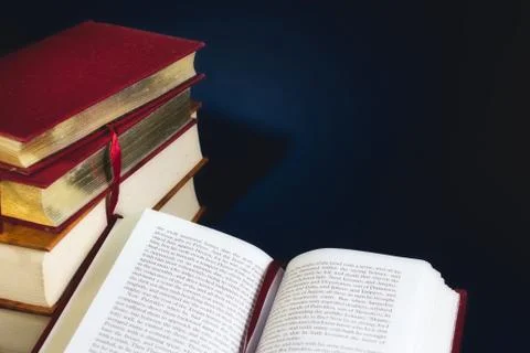 Stack of old books and an open book against a dark blue background Stock Photos