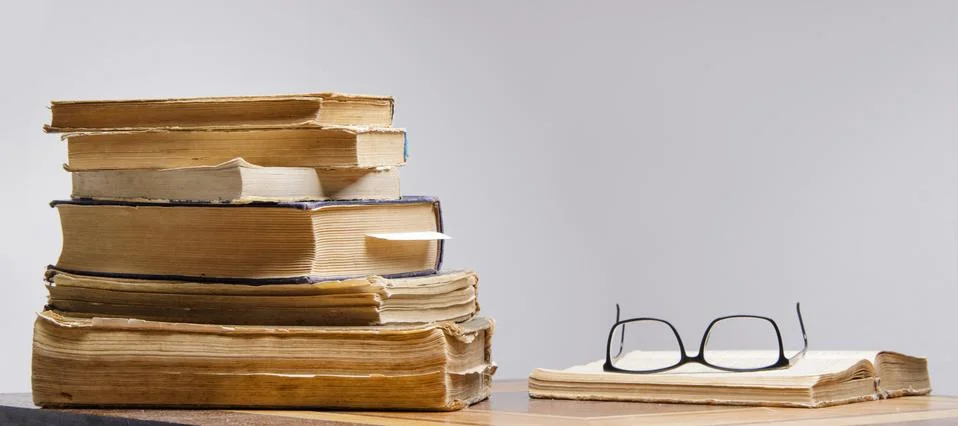 Stack of old books and reading glasses lie on the table Stock Photos
