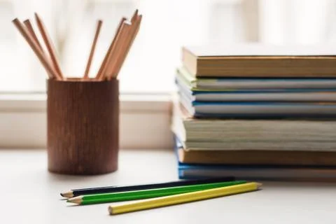 A stack of old books and several different colored pencils lie on the windows Stock Photos