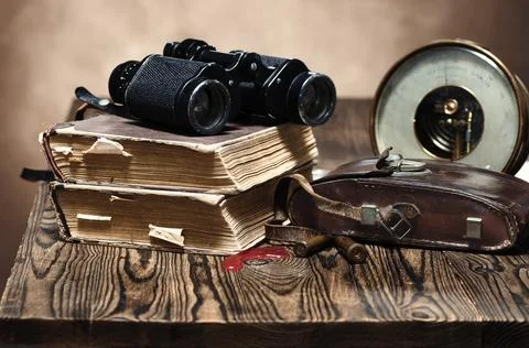 A stack of old books, binoculars, a barometer, a worn leather case and two Stock Photos