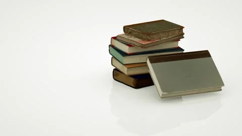 A stack of old books falls onto a white surface and is held in place, while the Stock Footage 155179250