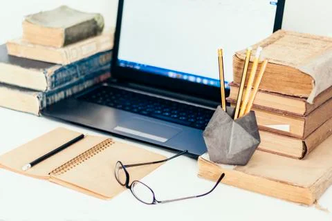 Stack of old books, laptop, glasses and notebook, retro office business backg Stock Photos