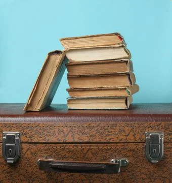Stack of old books on retro suitcase on a blue background. Stock Photos