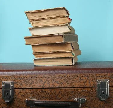 Stack of old books on retro suitcase on a blue background. Stock Photos