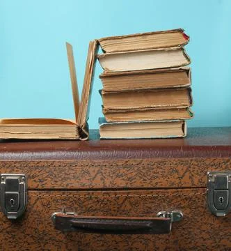 Stack of old books on retro suitcase on a blue background. Stock Photos