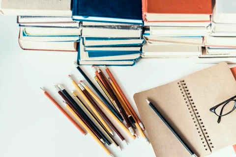 Stack of old books, textbook, notebook, glasses and pencils on white table in Stock Photos