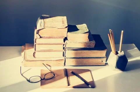 Stack of old books, textbook, notebook, glasses and pencils on white table in Stock Photos