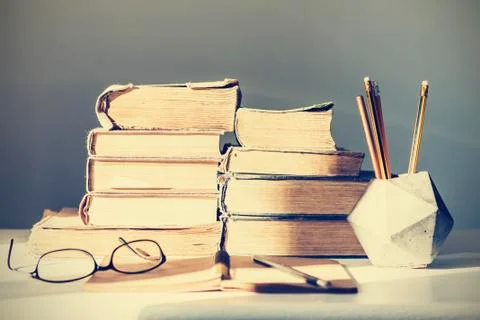 Stack of old books, textbook, notebook, glasses and pencils on white table in Stock Photos