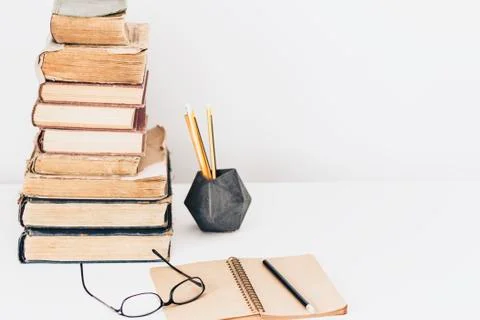 Stack of old books, textbook, notebook, glasses and pencils on white table in Stock Photos
