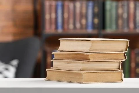 Stack of old books on white table with blurred library background, education  Stock Photos