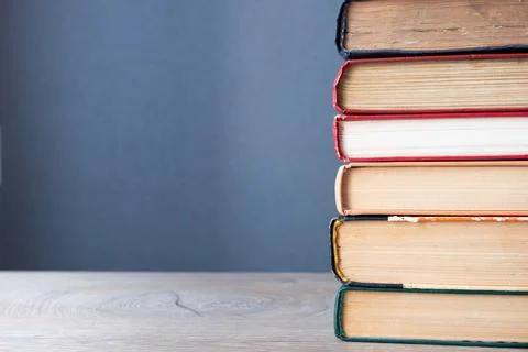 Stack of old books on wooden table and gray background with copyspace to left Stock Photos