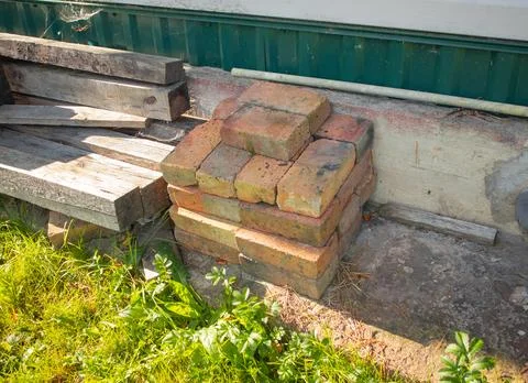 Stack of old bricks and wooden planks by house wall backyard materials Stock Photos
