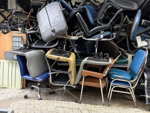 Stack of old broken office chairs stored outdoors Stock Photos