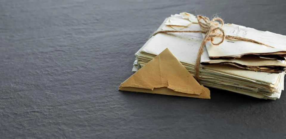 Stack of old torn vintage letters on yellowed paper against black granite t.. Stock Photos