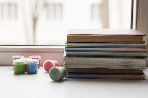 A stack of old various books and some color pencils lying on the windowsill,  Stock Photos