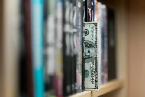 A stack of one hundred dollar bills sticking out of a bookshelf Stock Photos