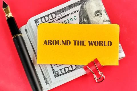 A stack of one hundred Dollar bills sits on a red surface, topped with a yellow Foto stock