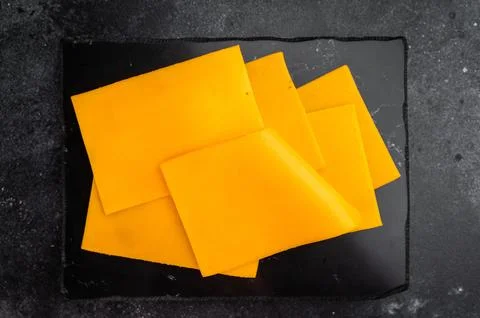 Stack of orange cheese slices on black stone background minimal food compos.. 스톡 사진