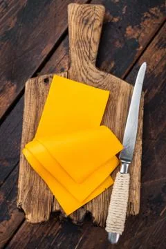 Stack of orange cheese slices on board with knife dark wooden background da.. Foto stock