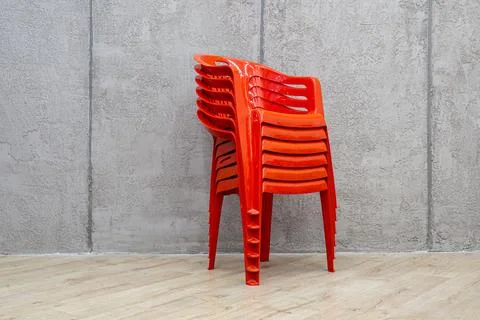 Stack of orange plastic chairs for commercial storage against concrete wall Stock Photos