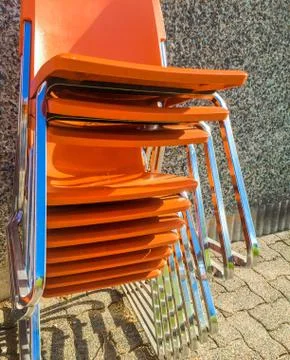 Stack of orange plastic modern chairs outside. Stock Photos