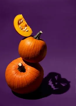 Stack of orange pumpkins with shadow of Jack on purple background. Balancing Stock Photos