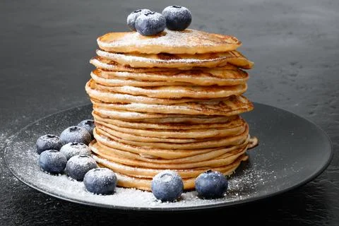 Stack of pancakes with blueberry and powdered sugar on black plate Stock Photos