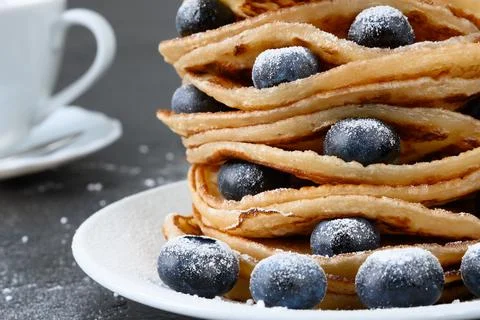 Stack of pancakes with blueberry and powdered sugar on white plate and teacup Foto stock
