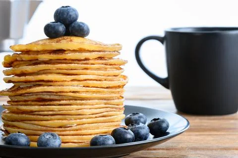 Stack of pancakes with blueberry, dark mug and coffee pot on wooden table Stock-Fotos