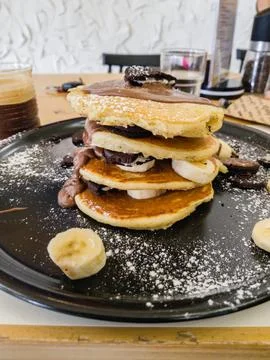 Stack of pancakes with chocolate spread, banana slices, and cookies, dusted.. 스톡 사진