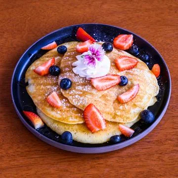 Stack of pancakes covered with blueberries and sliced strawberries and topped Stock Photos