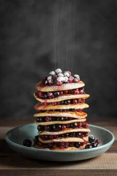Stack of pancakes with falling powdered sugar on wooden table Stock Photos