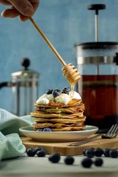Stack of pancakes with fresh blueberries and a hand with honey spoon above, c Stock Photos
