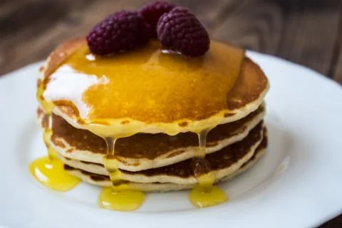 Stack of pancakes with honey and raspberry on white plate Stock Photos