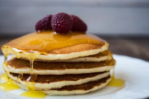 Stack of pancakes with honey and raspberry on white plate Stock Photos
