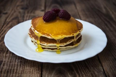 Stack of pancakes with honey and raspberry on white plate Stock Photos
