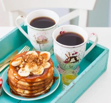 Stack of pancakes with maple syrup, chopped bananas and pecan nuts. Two cups Stock Photos