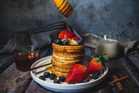 A stack of pancakes with pouring honey, fresh blueberry and strawberry and wh Stock Photos