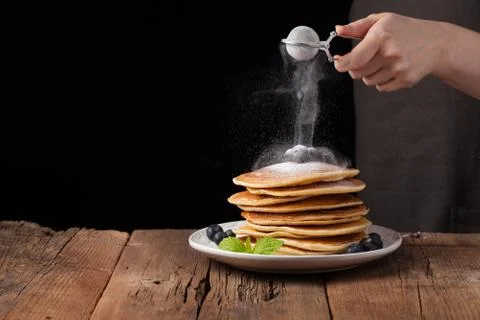Stack of pancakes with sugar powder splashes cooking by chef hand on wooden d Stock Photos